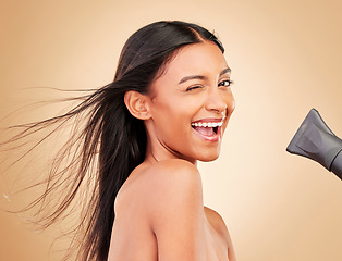 Image showing Wink, hair and portrait of happy woman with hairdryer for beauty isolated in a studio brown background with strong texture. Aesthetic, glow and young person with heat or wind for health and shine