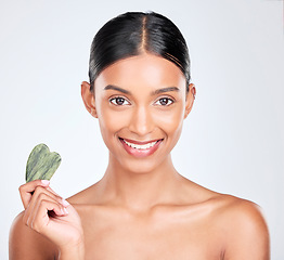 Image showing Portrait, beauty and gua sha face massage with a woman in studio on a white background holding a stone. Smile, skincare and facial with a happy young model looking confident at luxury wellness