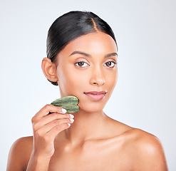 Image showing Portrait, skincare and gua sha facial massage with a woman in studio on white background holding a stone. Face, beauty and natural with a confident young model using antiaging jade to relax her skin