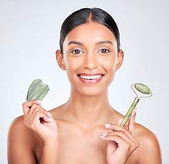 Image showing Portrait, beauty and gua sha facial massage with a woman in studio on a white background holding a stone. Smile, skincare and face roller with a happy young model looking confident at luxury wellness