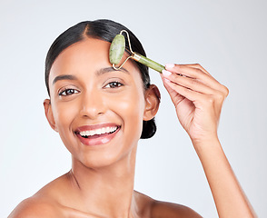 Image showing Portrait, beauty and facial massage roller with a woman in studio on a white background holding a stone. Face, smile and skincare with a happy young model looking confident at luxury wellness