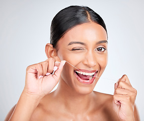 Image showing Woman, portrait and wink to floss teeth in studio for healthy dental care, gum gingivitis or plaque on white background. Face, happy indian model and oral thread for cleaning mouth, tooth and hygiene