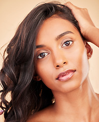 Image showing Hair care, beauty and face of woman in studio isolated on a brown background. Curly hairstyle, makeup cosmetics or portrait of serious Indian model in salon treatment for health, wellness or balayage