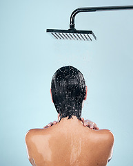 Image showing Woman, shower and back in water drops for washing, grooming or hygiene against a blue studio background. Rear view of female person in body wash, cleaning or skincare routine under rain in bathroom