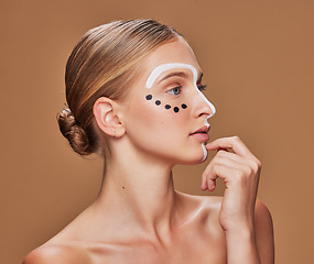 Image showing Face paint, woman and profile with skincare, dermatology and creative art in studio. Beauty, thinking and makeup with unique artwork and cosmetics with wellness of model with brown background