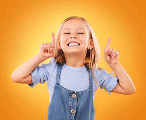 Image showing Child, happy portrait and pointing up in studio for advertising, announcement or promotion. Excited young girl kid on a orange background for hand gesture, sale or sign for attention or marketing