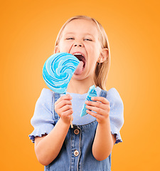 Image showing Lollipop, candy and portrait of a child in studio for sweets, color spiral or sugar for energy. Face of happy girl kid excited on orange background to lick or eating snack, dessert or unhealthy food