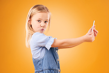 Image showing Phone, selfie or portrait of child in studio with confidence or mockup space in photograph memory. Kid, orange background or face of girl taking picture online on a social media app on internet