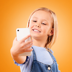Image showing Phone, selfie or face of child in studio with confidence or mockup space in photograph memory. Kid, orange background or happy girl taking picture online on a social media app to post on internet