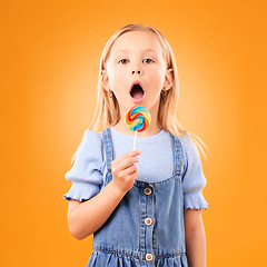 Image showing Candy, girl child and portrait of lollipop in hand, open mouth and studio for sweets, birthday party or carnival. Sugar, kid and eating spiral snack for dessert, hunger or meal on orange background