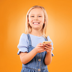 Image showing Child, portrait and typing with smartphone in studio for social media, play mobile games and smile on orange background. Happy girl kid, phone and reading notification, watch multimedia and tech app