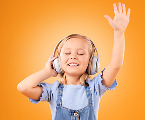 Image showing Headphones, happy or child streaming music to relax with freedom in studio on orange background. Hand up, singing or girl singer listening to a radio song, sound or gospel on an online subscription