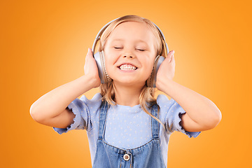 Image showing Headphones, smile or child streaming music to relax with freedom in studio on orange background. Face, singing or happy girl singer listening to a radio song, sound or audio on an online subscription