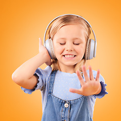 Image showing Headphones, dancing or child streaming music to relax with freedom in studio on orange background. Smile, excited and happy girl listening to a radio song, sound or audio on an online subscription