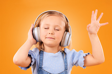 Image showing Child, headphones and dance to music in studio for freedom, multimedia subscription or kids podcast on orange background. Happy young girl listening to audio, streaming sound or hearing song on radio