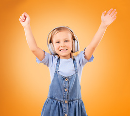 Image showing Portrait, child and dance with headphones in studio for freedom, music and excited party on orange background. Happy girl with energy listening to audio, streaming sound and celebrate song on radio