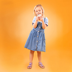 Image showing Girl, child and typing with phone in studio for social media, play mobile games and download app on orange background. Young kid scroll smartphone to search website, watch multimedia and subscription