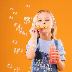 Image showing Portrait, child and blowing bubbles in studio for fun, freedom and childhood development on orange background. Young girl, kid and learning to play with soap bubble wand, toys and activity games