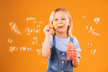 Image showing Portrait, happy child and blowing bubbles in studio for fun, freedom and childhood development on orange background. Girl, kid and smile for playing with soap bubble wand, toys and activity games