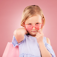 Image showing Girl, kid and portrait, fashion sunglasses with shopping bag or gift with event isolated on pink background. Stylish, retro and accessory with funky outfit, present for party or retail in studio