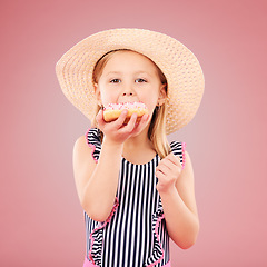 Image showing Girl kid, eating a donut and dessert, sweets and summer with hat and bathing suit isolated on pink background. Portrait, youth and cake with snack, child enjoying bakery treat with hat in studio