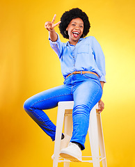 Image showing Black woman, peace and sign with hands on chair in studio, yellow background or natural happiness with casual fashion and style. African, gen z or model smile and relax for creative, mockup or space