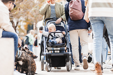 Image showing Mother walking and pushing his infant baby boy child in stroller in crowd of people wisiting sunday flea market in Malaga, Spain.