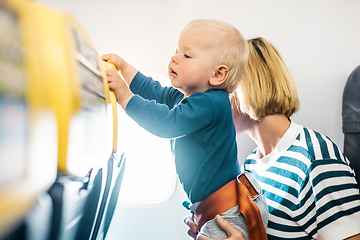 Image showing Mom and child flying by plane. Mother holding and playing with her infant baby boy child in her lap during economy comercial flight. Concept photo of air travel with baby. Real people.