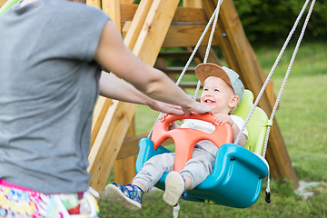 Image showing Mother pushing her infant baby boy child on a swing on playground outdoors.