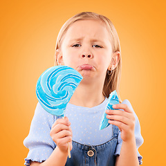 Image showing Portrait, children and sad girl with a broken lollipop on an orange background in studio looking upset. Kids, candy and unhappy with a female child holding a cracked piece of a sugar snack in regret