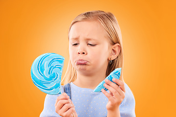 Image showing Children, candy and a sad girl with a broken lollipop on an orange background in studio looking upset. Kids, sweets and unhappy with a female child holding a cracked piece of a sugar snack in regret