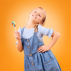 Image showing Happy, lollipop and girl child with candy, hungry for dessert .and isolated on an orange background in studio. Smile, sweets and young kid with sugar, unhealthy food and eating confectionery treats