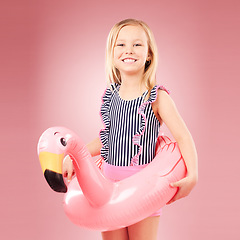 Image showing Girl child, summer and swimsuit with inflatable, flamingo and happiness with vacation on pink background. Swimwear, fun and animal toys, happy kid in portrait and playful with holiday in studio