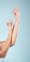 Image showing Water drops, hands and person closeup with cleaning, shower and morning dermatology in studio. Blue background, arm and splash for wellness, washing and skin glow with self care and hygiene safety