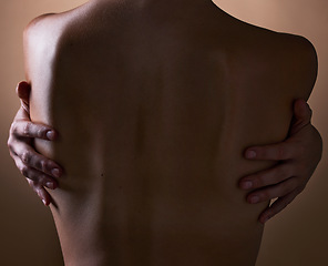 Image showing Woman, back and hands touching body on brown background in studio for creative aesthetic, art deco and skin texture. Person, dark and shadow of model in self love hug for nude and sensual wellness