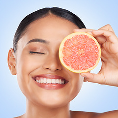 Image showing Face, skincare and grapefruit with a natural woman in studio on a blue background for health or wellness. Beauty, smile and aesthetic with a happy young model holding fruit for detox or antioxidants