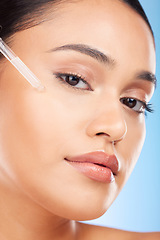 Image showing Woman, portrait and essential oil for beauty, skincare and cosmetics product on a blue background. Young person with facial serum, dermatology dropper or collagen for skin care on face in studio