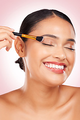 Image showing Happy, eyeshadow and a woman with a brush on a pink background for skincare, wellness and health. Smile, young and a female model with makeup, beauty or foundation on face for cosmetics on a backdrop