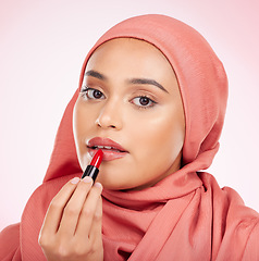 Image showing Portrait, beauty or lipstick with an arab woman closeup in studio on a pink background for cosmetics. Face, makeup and muslim with a confident young model in an hijab to apply a product for red color