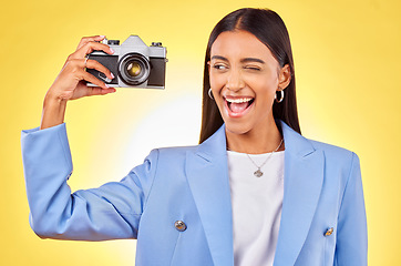 Image showing Camera, photography and woman picture with a smile and wink for job in studio. Happy, young female person and yellow background with creative, memory and funny emoji face with photographer skill