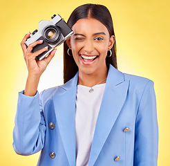 Image showing Camera, photography and woman portrait with a smile and wink for picture in studio. Happy, female person and yellow background with creative, memory and funny emoji face with photographer skill