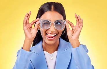 Image showing Funny, silly woman and sunglasses with tongue out, comedy and face in a studio. Yellow background, crazy and young female person with modern fashion, trendy cool style and creative work clothing