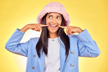 Image showing Fashion, smile and face of Indian woman on yellow background with silly, goofy and playful expression. Emoji, happiness and person in studio pointing to mouth in trendy accessories, style and hat