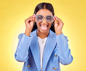 Image showing Funny, woman smile and sunglasses with tongue out, comedy and silly face in a studio. Yellow background, crazy and female person with modern fashion, trendy cool style and creative work clothing