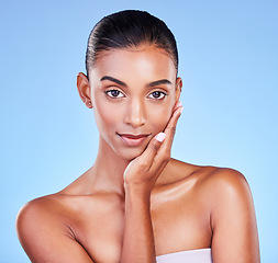 Image showing Skincare, woman and hand on face in studio for wellness, cosmetic or treatment on blue background. Portrait, beauty and lady model touching glow, skin or smooth, dermatology or results satisfaction