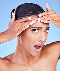 Image showing Shock, pimple and young woman in studio for cosmetic, beauty and natural face routine. Health, wellness and Indian female model with acne skin on forehead for facial dermatology by a blue background.