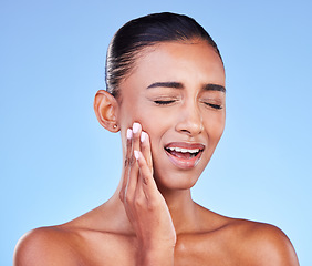 Image showing Dental hygiene, pain and woman with toothache, cavity and plaque on a blue studio background. Person, girl and model with oral care, touching her sore cheek and medical issue with emergency or crisis
