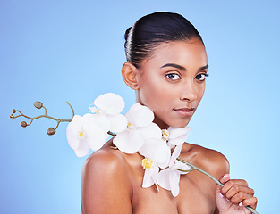 Image showing Natural beauty, woman and face, flower and glow with wellness and eco friendly dermatology isolated on blue background. Sustainable skincare, orchid with collagen and cosmetics in portrait in studio