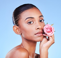 Image showing Rose, portrait and skincare of woman on blue background for eco cosmetics, natural glow and aesthetic in studio. Face, indian model and flowers for vegan beauty, sustainability or floral dermatology