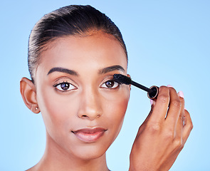 Image showing Face, makeup and woman with mascara, brush and beauty with skin glow isolated on blue background. Eyelash extension, cosmetics product and Indian model in portrait with cosmetology in a studio
